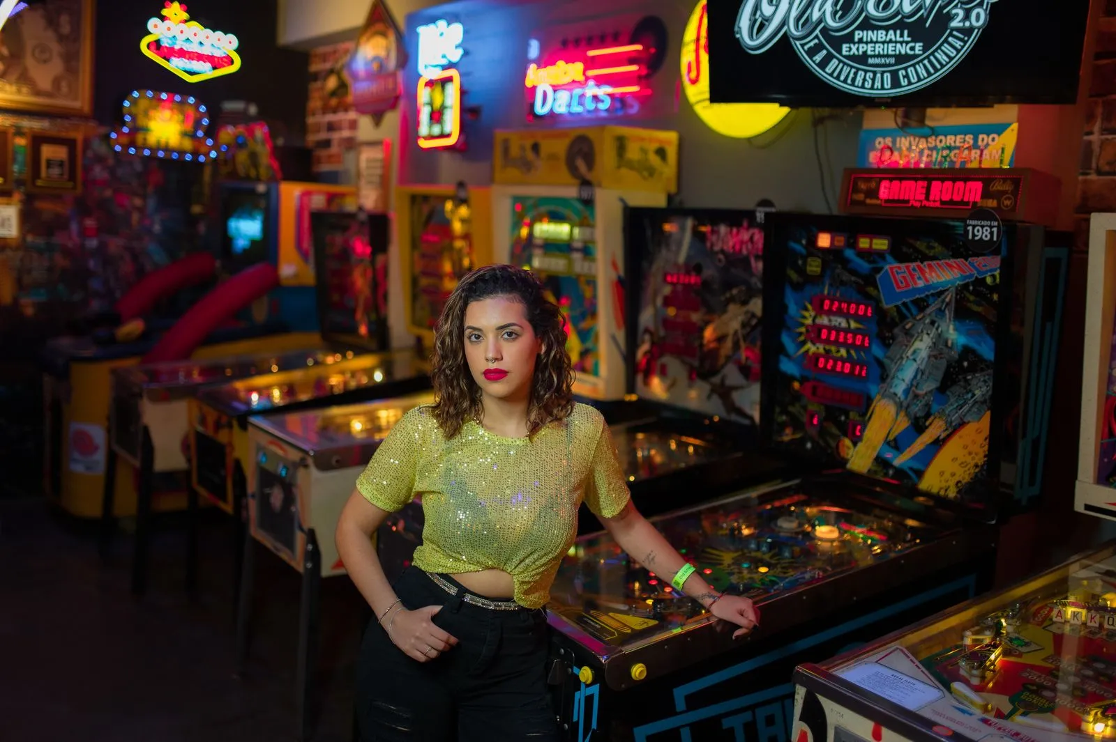 A fashionable woman stands confidently in a vibrant vintage arcade setting.